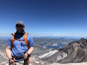 Thomas at the summit after climbing Mount Saint Helens. Spirit Lake and Mount Rainier in the distance.