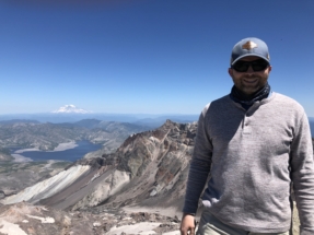 Thomas at the summit of Mount Saint Helens with Spirit Lake and Mount Rainier in the distance.