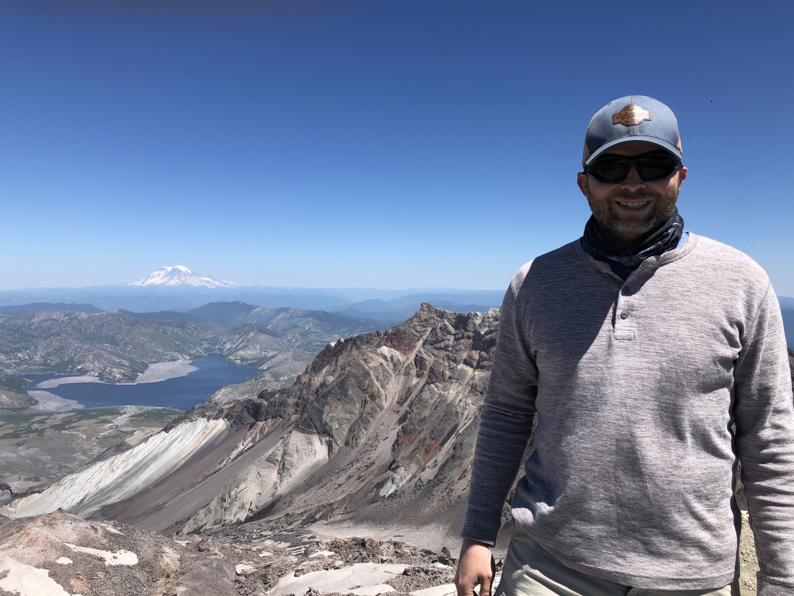 Thomas at the summit of Mount Saint Helens with Spirit Lake and Mount Rainier in the distance.